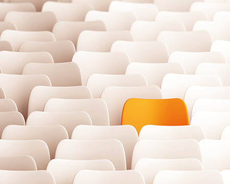 Ein orangefarbener Stuhl zwischen vielen weißen Stühlen